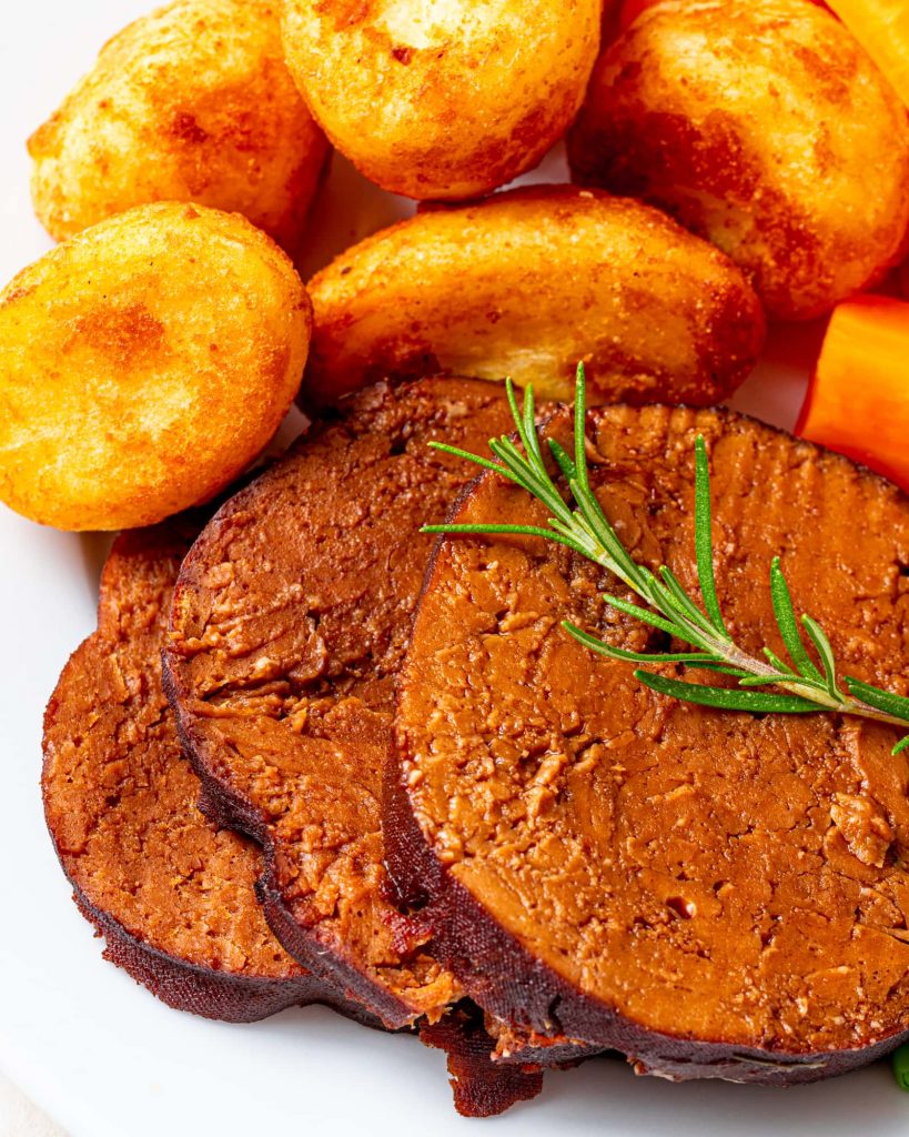 Vegan beef sliced made from seitan served on a plate with roast potatoes and carrots. 
