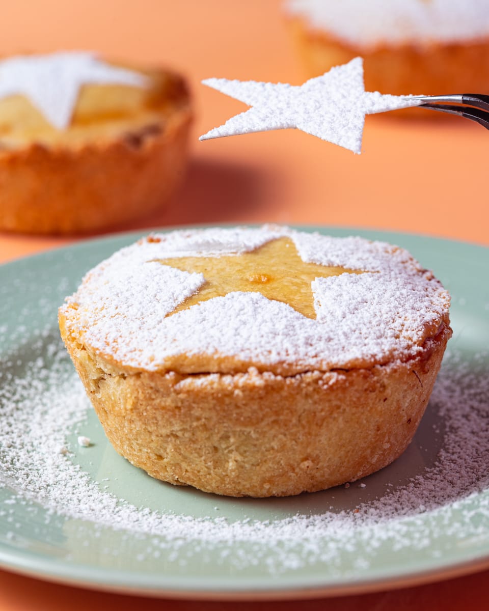 Using a paper stencil to make patterns on a vegan mince pie with powdered sugar. 