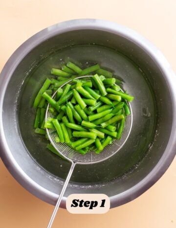 the first step in the process of making green bean casserole: the image shows the cooked green beans being blanched in ice cold water to stop them from cooking. 