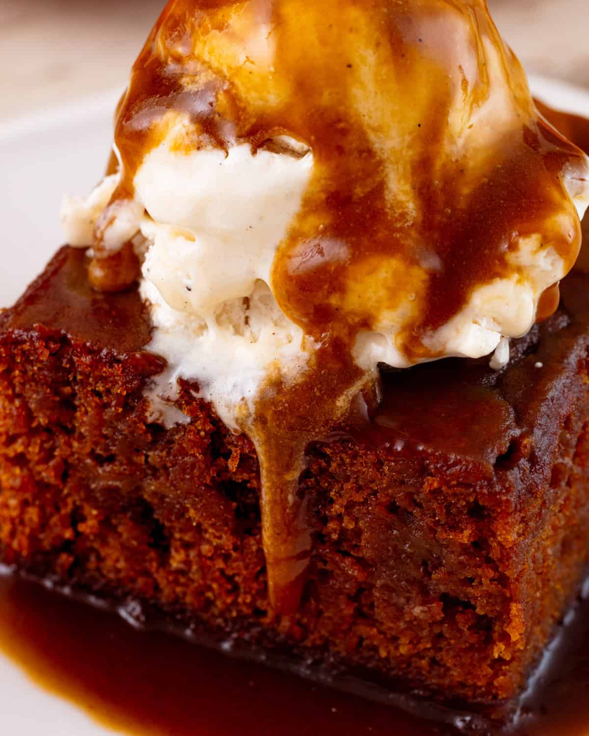 Melting ice cream and runny toffee sauce on top of a vegan sticky toffee pudding slice.