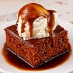A slice of warm vegan pumpkin sticky toffee pudding on a plate with a scoop of ice cream and topped with hot toffee sauce.