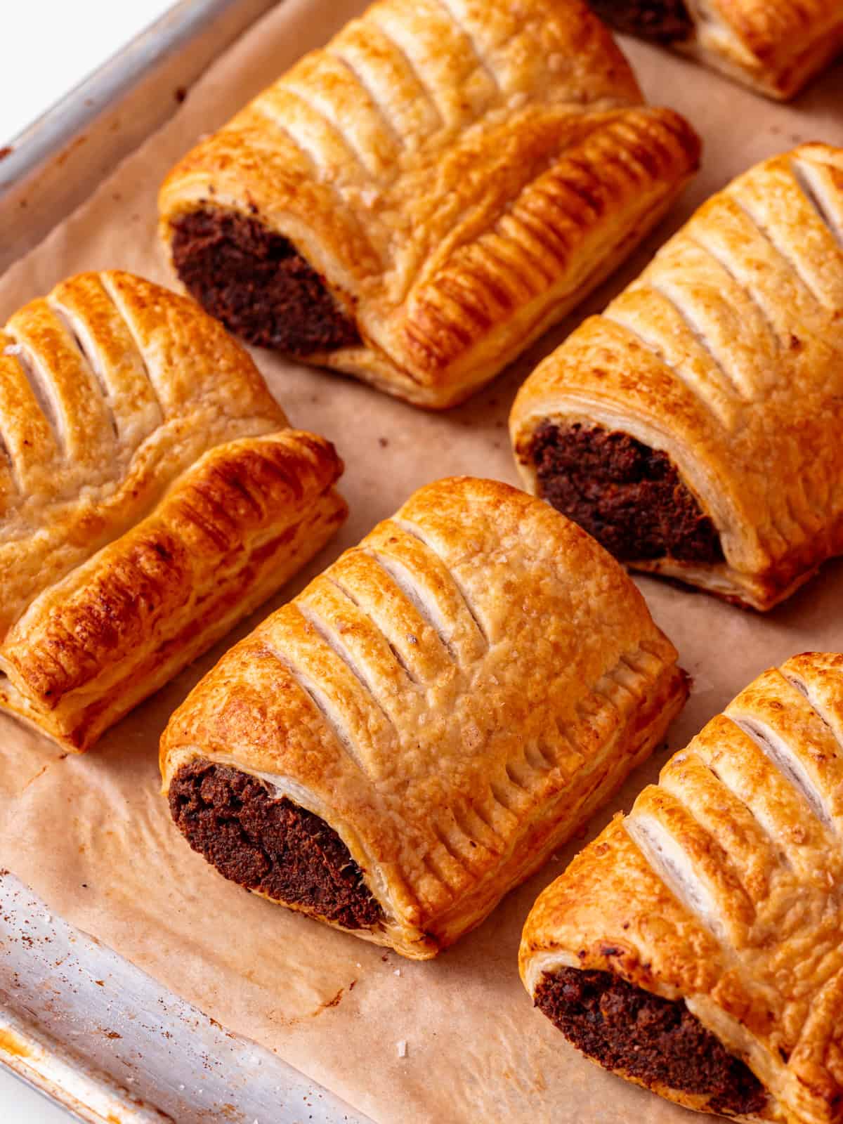 A tray of golden brown flaky puff pastry vegan sausage rolls. They're sat in rows on baking parchment.