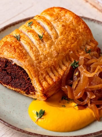 a vegan sausage roll on a plate with mustard and caramelised onions