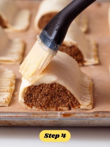 Vegan sausage rolls being brushed with egg wash before being baked.