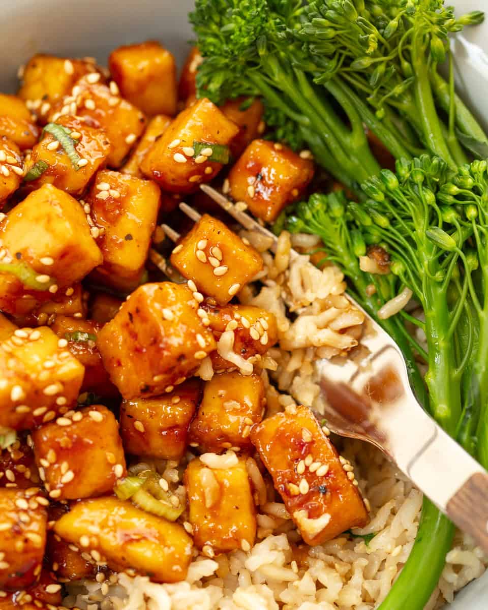 Sticky sesame tofu in a bowl with brown rice and broccoli